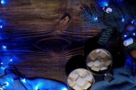 Christmas hot drink. Cocoa with marshmallow, garland and spruce branches on a wooden background. Top viewの写真素材