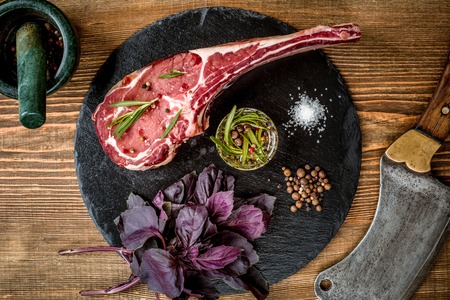 Dry aged raw tomahawk beef steak with ingredients for grillingの写真素材
