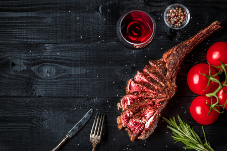 Barbecue dry aged rib of beef with spice, vegetables and glass of red wine close-up on black wooden backgroundの写真素材