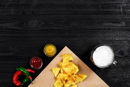 Snack for party, chips, nachos with sauces: tomato ketchup , mustard and mug of beer on a black background. Top view, copy spaceの写真素材