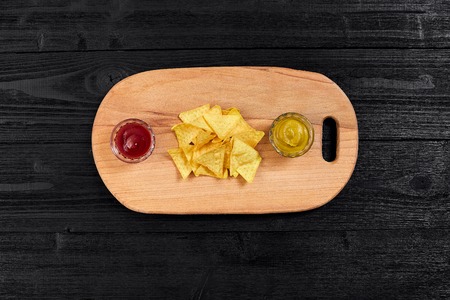 Tortilla chips with mustard and tomato sauce on black wooden table. Top viewの写真素材