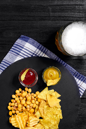 Overhead view of beer glass and snacks with sauce on black wooden table.の写真素材