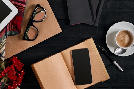 Above view of Smart phone with notebook and cup of latte coffee on black wooden background.