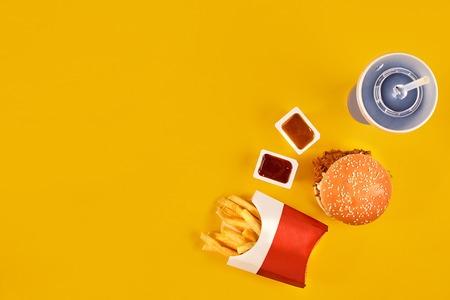 Fast food dish top view. Meat burger, potato chips and wedges. Take away composition. French fries, hamburger, mayonnaise and ketchup sauces on yellow background.の写真素材