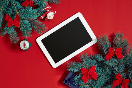 Christmas decorations and white tablet with black screen on hot red background. Christmas and New Year theme. Place for your text, wishes, logo. Mock up.の写真素材