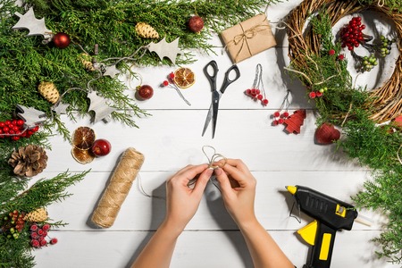 Christmas handmade diy background. Making craft xmas wreath and ornaments. Top view of white wooden table with female hands.の写真素材