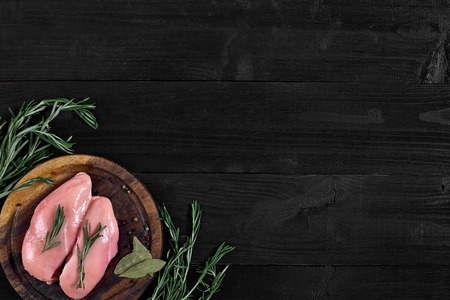 Raw chicken breast and condiments in a rustic wooden setting, top view