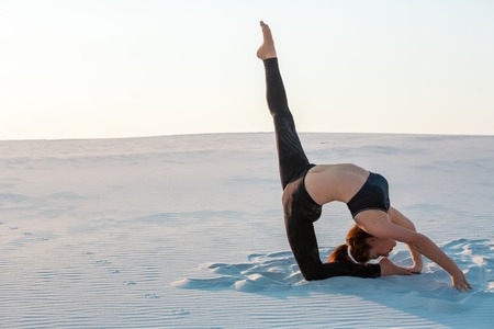 Fitness yoga woman stretching on sand. Fit female athlete doing yoga pose.の写真素材