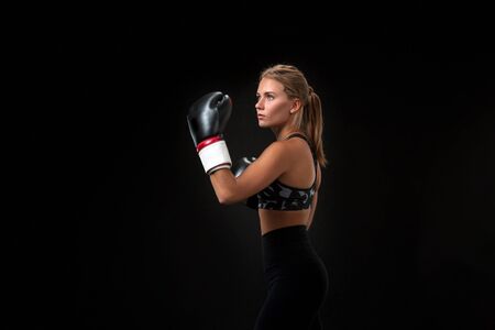 Beautiful female athlete in boxing gloves, in the studio on a black background.の写真素材