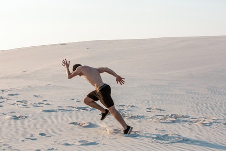 Fit man running fast on the sand. Powerful runner training outdoor on summer.