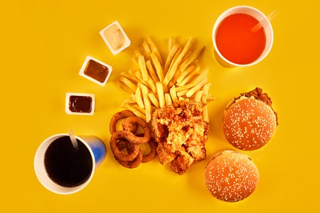 Fast food concept with greasy fried restaurant take out as onion rings, burger, fried chicken and french fries as a symbol of diet temptation resulting in unhealthy nutrition.の写真素材