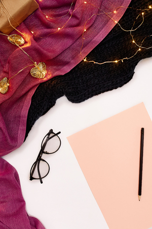 Black glasses, pink paper with new years goals. Scarf and Christmas lights on white background.の写真素材