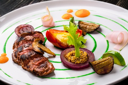 Sliced meat with fresh herbs, vegetables and spices on a white plate on a black wooden background, top viewの写真素材