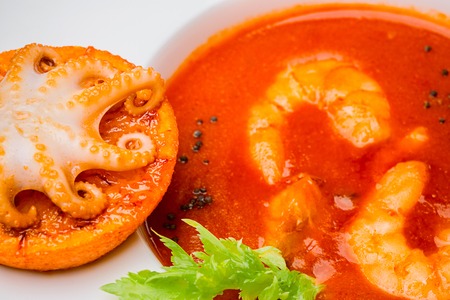 Bowl of tomato soup with shrimps with a small octopus baked on an orange slice. Close-up, top view