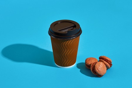 Hot coffee in brown paper cup with black lid and macaroons on blの写真素材