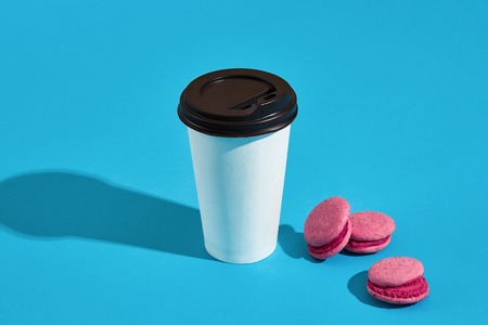 Hot coffee in white paper cup with black lid and pink macaroonsの写真素材