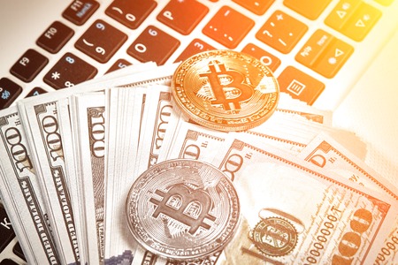Bitcoins with dollar bills on laptop keyboard. Sun flareの写真素材