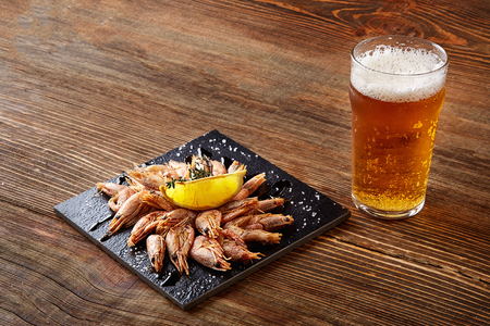 Grilled shrimps on black board pan and beer on wooden tableの写真素材