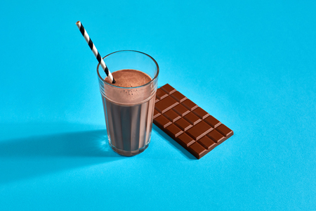 Glass of chocolate milk with chocolate bar on blue background with space for text or designの写真素材