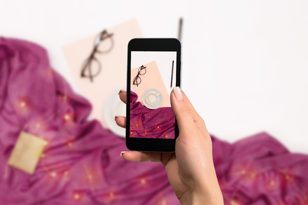 Female hand with a smartphone makes a photo workspace with notebook, coffee cup, scarf, glasses.の写真素材