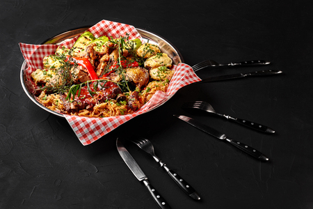 Assorted delicious grilled meat with vegetables and bbq sauce on an iron tray on black background close up. Big set of Hot Meat Dishes. Top viewの写真素材