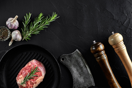 Fresh raw meat. A piece of beef tenderloin on grill pan, with a cutting ax, with spices for cooking on black stone table. Copy spaceの写真素材