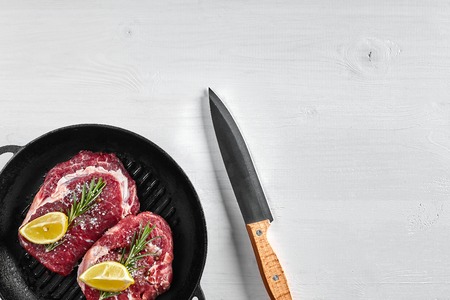 Raw Steak in grill frying pan with herbs and oil on white background, top view, place for text. Copy space. Still life. Flat layの写真素材