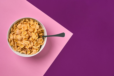 Bowl with corn flakes and spoon on purple and pink background, top viewの写真素材