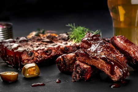 Pork ribs in barbecue sauce and a glass of beer on a black slate dish. A great snack to beer on a dark stone background. Top view with copy spaceの写真素材