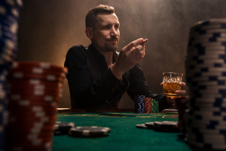 Young handsome man sitting behind poker table with cards and chipsの写真素材