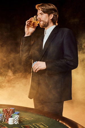 A man in a business suit standing near the game table. Male player. Passion, cards, chips, alcohol, dice, gambling, casino - it is as male entertainment.の写真素材