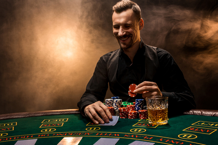 Man is playing poker with a cigar and a whiskey. A man winning all the chips on the table with thick cigarette smoke.の写真素材