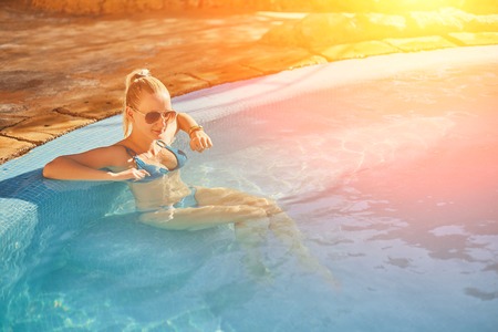 Woman in blue swimsuit and sunglasses relaxing in outdoor pool with clean transparent turquoise water. Sun flareの写真素材