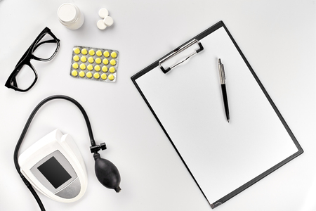 Top view of doctors desk table, blank paper on clipboard with pen, electronic manometer to measure the blood pressure.の写真素材