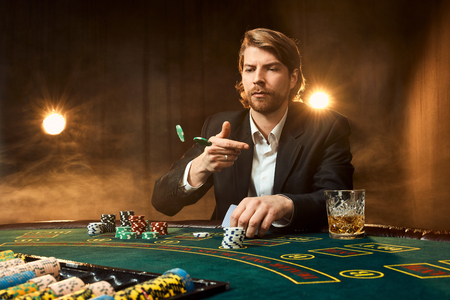 A man in a business suit sitting at the game table. Male player. Passion, cards, chips, alcohol, dice, gambling, casino - it is as male entertainment.の写真素材