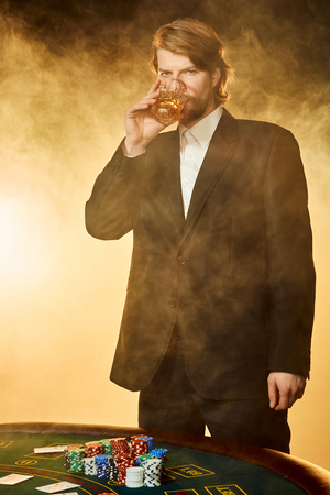 A young man in a business suit standing near poker table. Man gambles.の写真素材