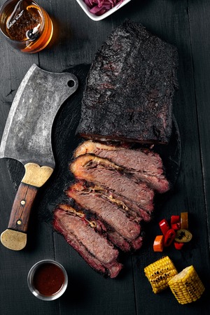 Fresh Brisket BBQ beef sliced for serving against a dark background with sauce, hot peppers and corn. Generous accommodation for copy space. American styleの写真素材