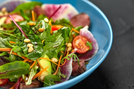Spicy beef slices meat salad with tomatoes, parsley, radish and salad leaves spinach in a blue plate on a black table. Close-upの写真素材