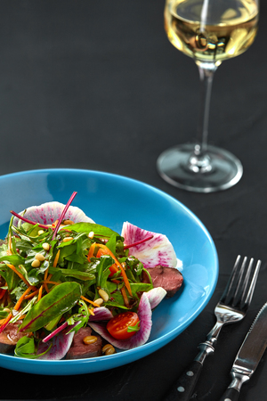 Spicy beef slices meat salad with tomatoes, parsley, radish and salad leaves spinach on black texture background tableの写真素材