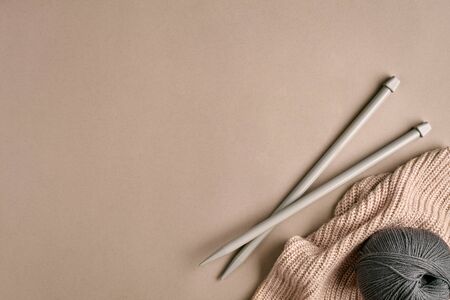 Knitted from a gray yarn sweater and thread for knitting closeup. Knitting as a hobby. Accessories for knitting on a beige background. Top view. Still life. Copy space. Flat layの写真素材