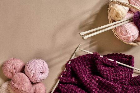 Balls of merino wool yarn, knitting on knitting needles on a beige surface. Pink, white and purple ball of thread in the basket. Top view. Still life. Copy space. Flat layの写真素材