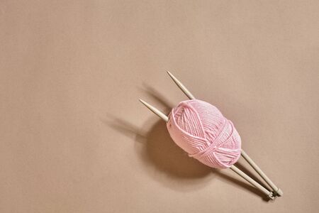 Pink knitting yarn ball and knitting needles on a beige background. Top view. Copy space. Still...