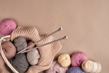 Different colored yarn in basket with knitting needles on a beige background. Top view. Copy space....
