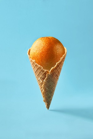 Orange like ice cream lies in waffle cone on a light blue background.の写真素材