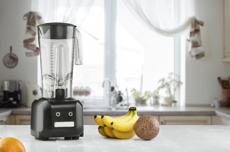 Metal food blender close-up with fresh exotic tropic fruits next to it on kitchen background with empty space. Sun flareの写真素材