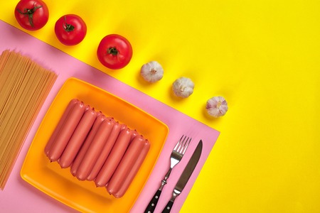 Sausages with tomatoes, spaghetti and garlic on a yellow and pink minimal background. Flat lay. Top view.の写真素材