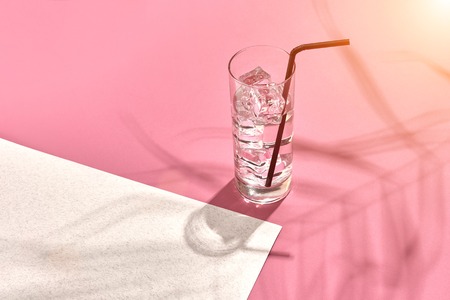 Glass of mineral water with ice on pink and white background with shadow from a palm leaf. Top view. Still life. Copy space. Flat lay. Sun flareの写真素材