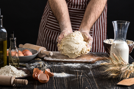 Against the background of mens hands knead the dough. Ingredients for cooking flour products or dough bread, muffins, pie, pizza dough .の写真素材