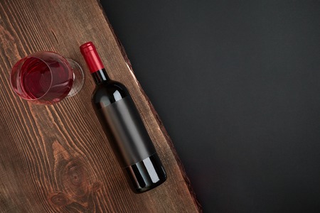 Bottle of wine and one glass on the wooden board on black background. Top view with copy space. Still life. Flat layの写真素材