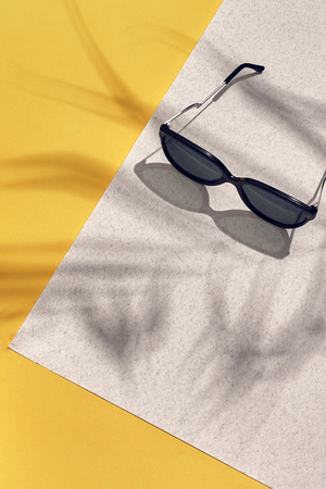 Stylish sunglasses with bright sunlight and shadow from palm leaves. Summer vacation concept.の写真素材